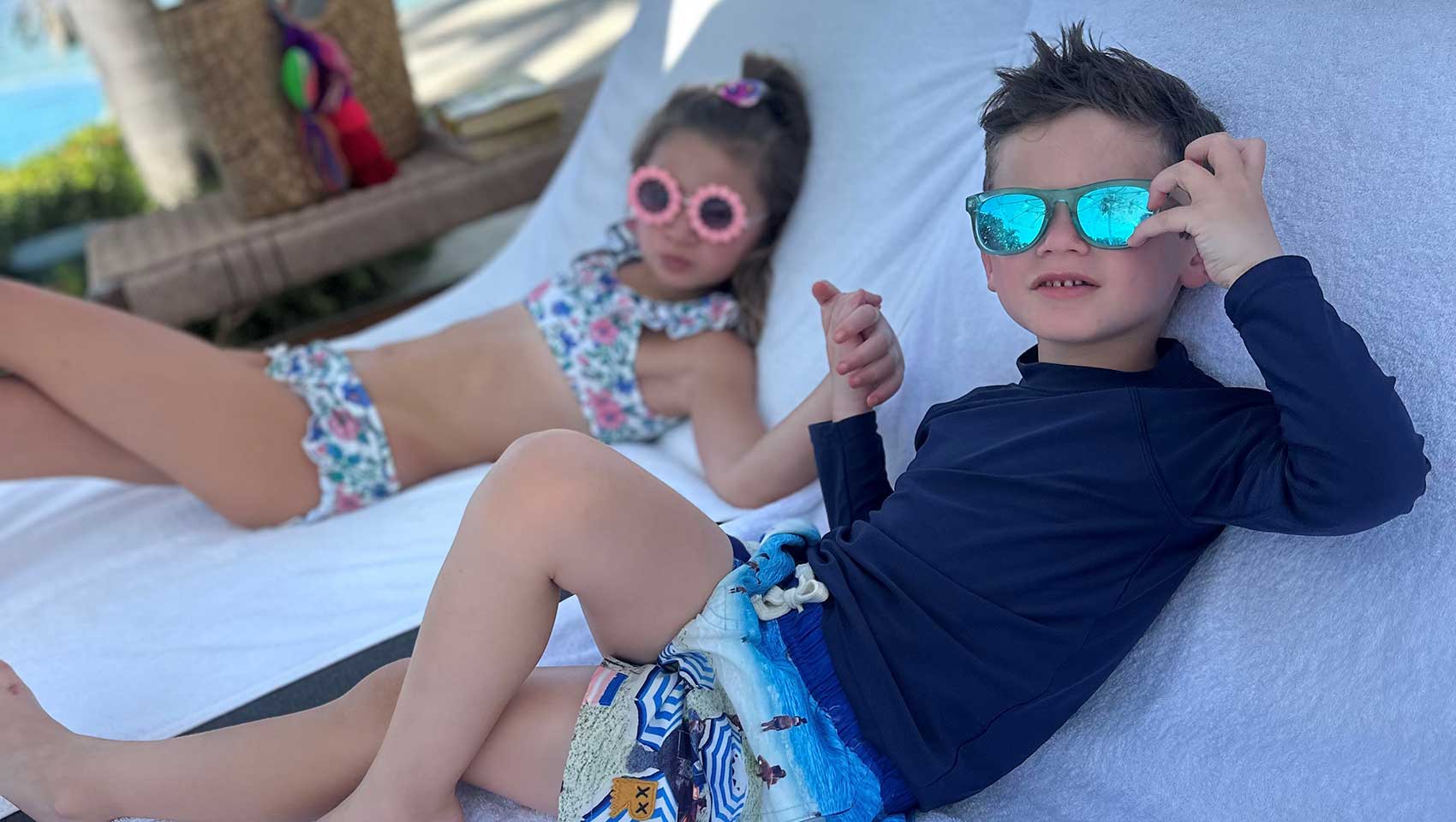 two kids in sunglasses relaxing on beach loungers