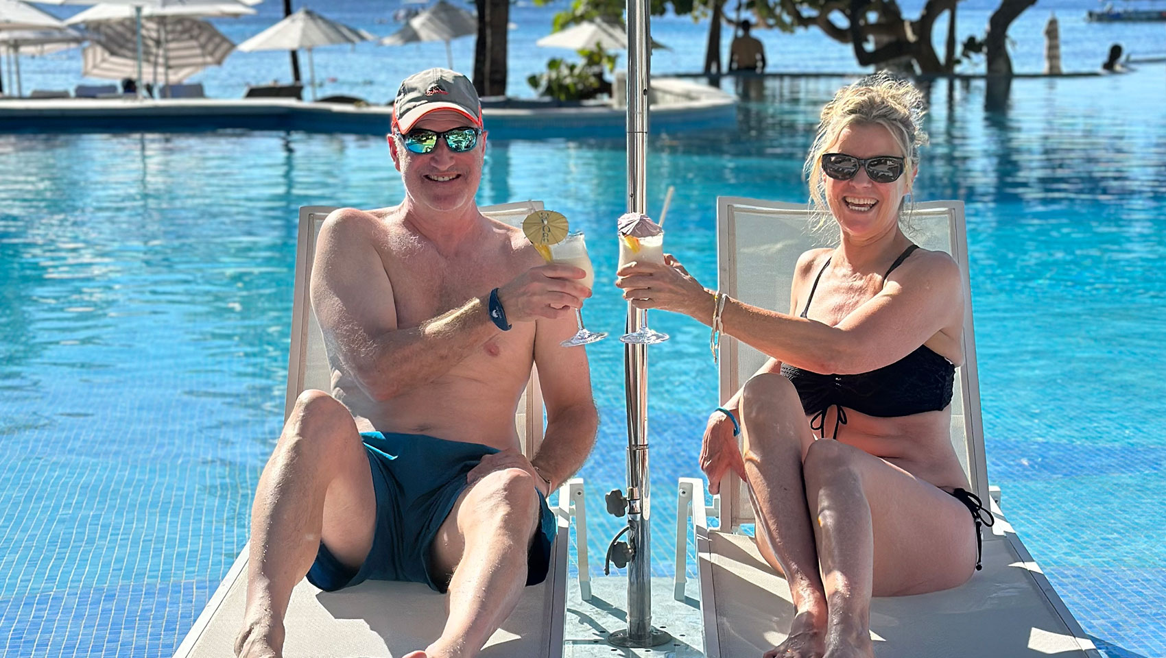 Couple sitting under umbrella by the pool at Kimpton Grand Roatan with cocktails