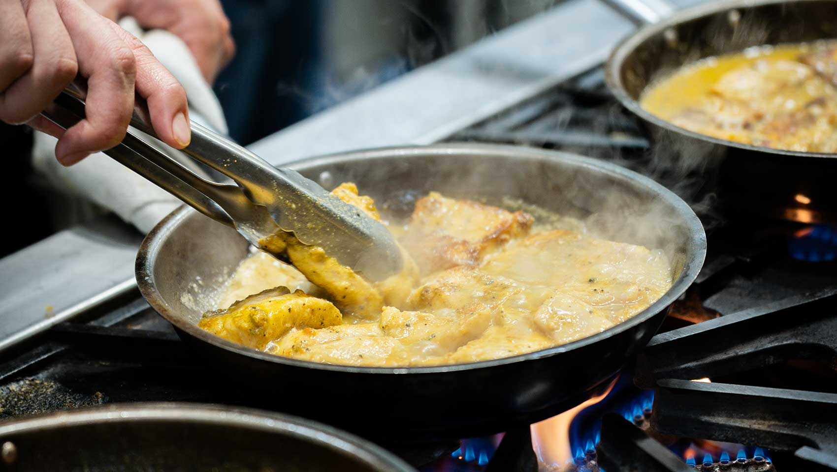 Chef uses tongs while cooking a saucy dish at Kimpton Grand Roatan